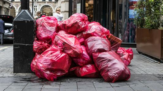 Red bags of rubbish sit on the sidewalk of a nice street.