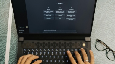 First person view of a woman typing a question into ChatGPT on her laptop.