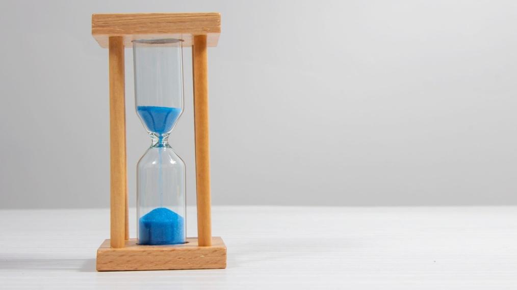 Hour glass with blue sand dripping down, about half of it has dropped into the bottom.