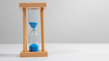 Hour glass with blue sand dripping down, about half of it has dropped into the bottom.