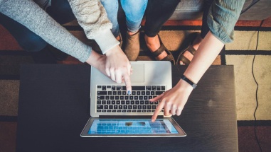 Group of people around a desk pointing at a laptop.