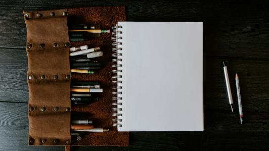One notebook page with pencils and pens around it.