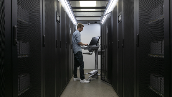 Man working on computer in a datacentre surrounded by racks.