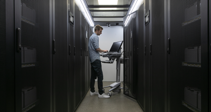 Man working on computer in a datacentre surrounded by racks.